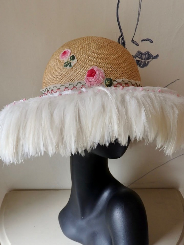 Straw hat with pink flowers and white feathers flowing from the brim.