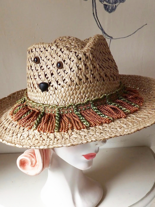 Straw hat with brown and green tassels and a face made from buttons.