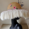 Straw hat with pink flowers and white feathers flowing from the brim.
