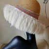 Straw hat with pink flowers and white feathers flowing from the brim.